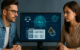 Man and woman next to Monitor displaying AI and a dashboard.